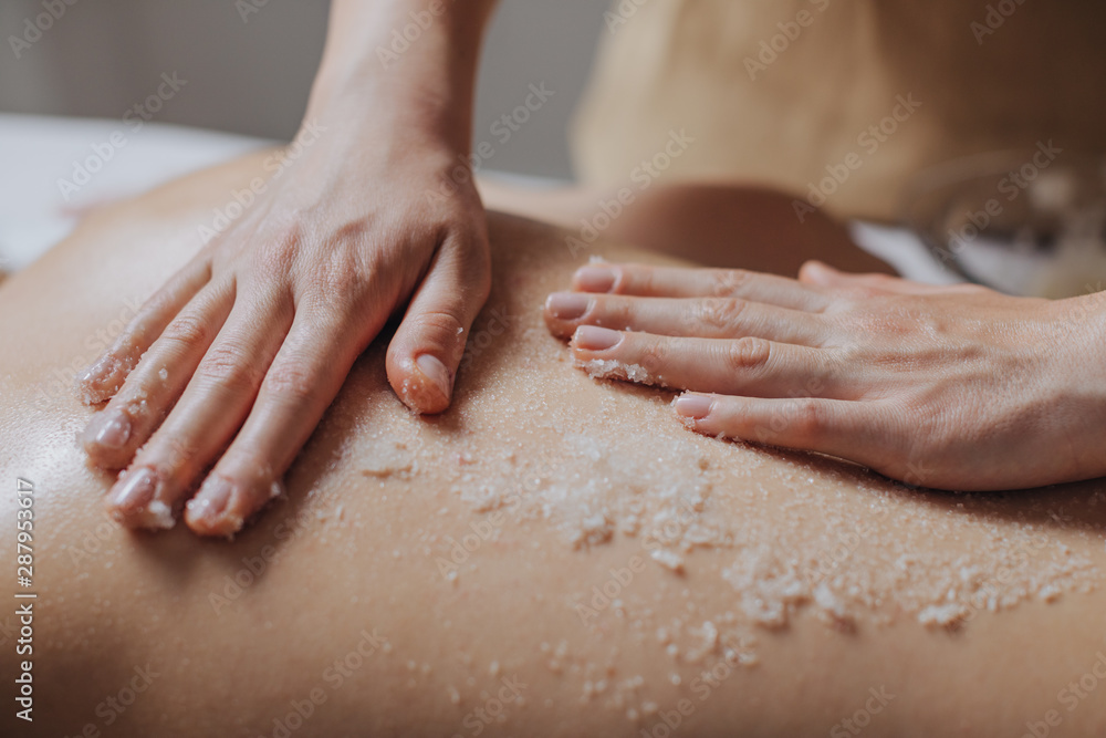 Hands of unrecognisable woman masseuse applying skin scrub on client's back. Hands of unrecognisable woman masseuse applying skin scrub on client's back.