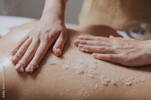 Hands of unrecognisable woman masseuse applying skin scrub on client's back. photo