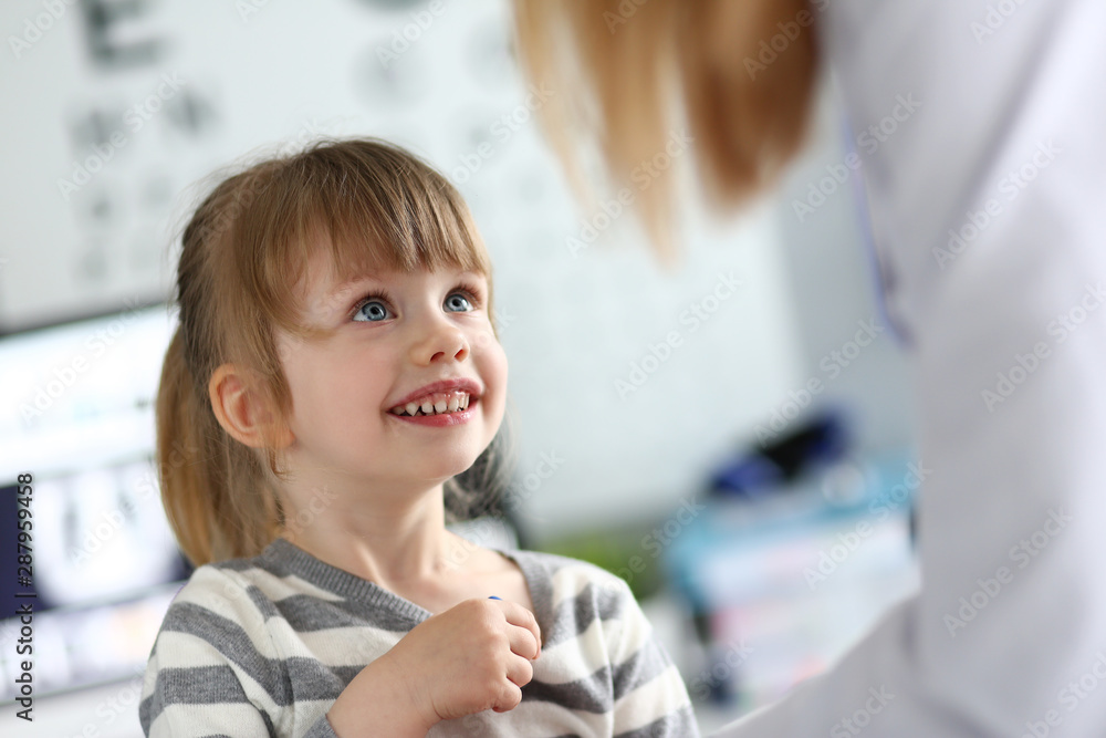 Portrait of smiling little girl looking at doctor with happiness. Nice joyful baby visiting family doc. Health care and prevention concept. Blurred background Portrait of smiling little girl looking at doctor with happiness. Nice joyful baby visiting family doc. Health care and prevention concept. Blurred background