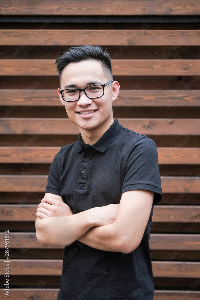 A young korean man in a black t-shirt. Asian man with glasses on a wooden background. A young korean man in a black t-shirt. Asian man with glasses on a wooden background.