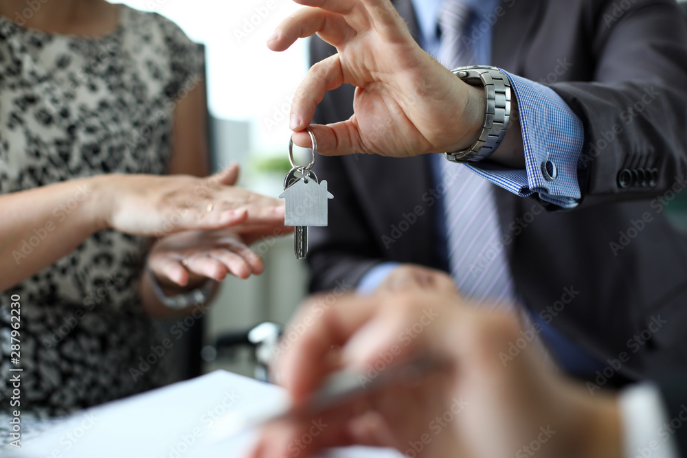 Obraz premium Focus on male hand with home keychain. Customer signing profitable contract of property purchase and sale. Businesswoman applauding. Real estate market and business concept. Blurred background