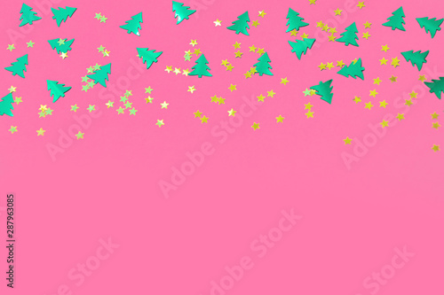 Green metallic foil christmas trees and gold stars confetti sparse on pink background. Simple holiday concept. Design template. Frame with copy space. Winter festive backdrop. Top view, flat lay.