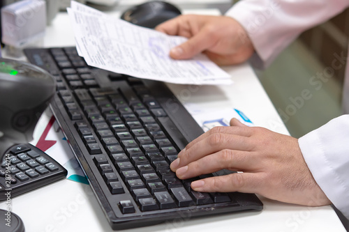 Male medicine doctor hands hold recipe and type something on a laptop computer keyboard. Panacea and life saving. Pharmacist with a prescription in hand