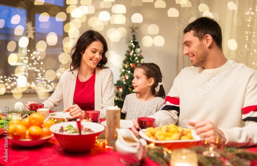 holidays, family and celebration concept - happy mother, father and little daughter having christmas dinner at home © Syda Productions