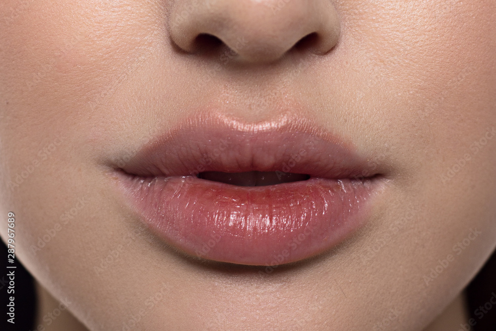 Fototapeta premium Cosmetics, makeup and trends. Bright lip gloss and lipstick on lips. Closeup of beautiful female mouth with natural lip makeup. Beautiful part of female face. Perfect clean skin in red light