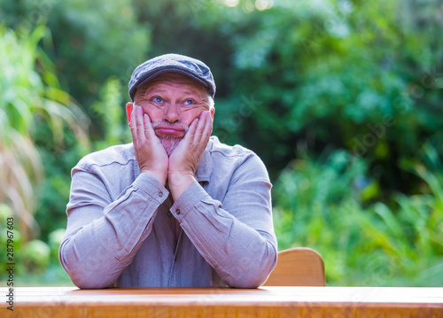 An elderly man is sitting at a table in the garden. He is bored and has nothing to do. photo