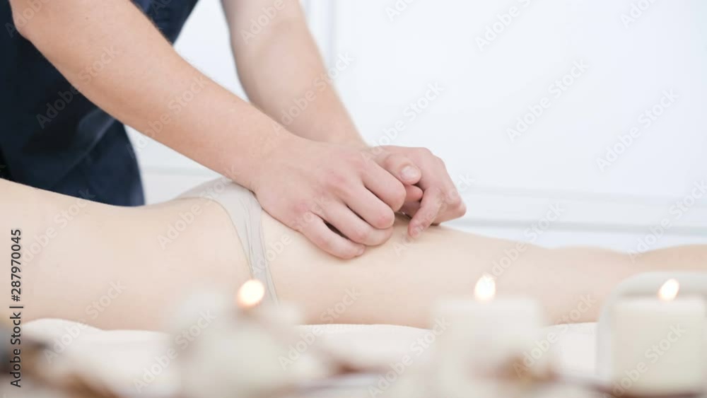 Close-up of a male physiotherapist doing a light massage to warm up the hips and buttocks of a young woman in a professional spa salon next to a sprig of cotton. 4K massage body care concept Close-up of a male physiotherapist doing a light massage to warm up the hips and buttocks of a young woman in a professional spa salon next to a sprig of cotton. 4K massage body care concept