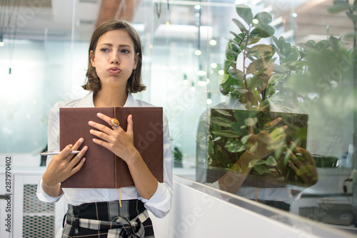 Photography Portrait of beautiful young business woman pouting and holding notebook in offic