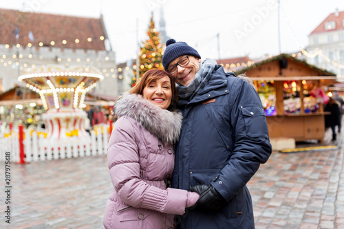 love, winter holidays and people concept - happy senior couple hugging at christmas market on town hall square in tallinn, estonia