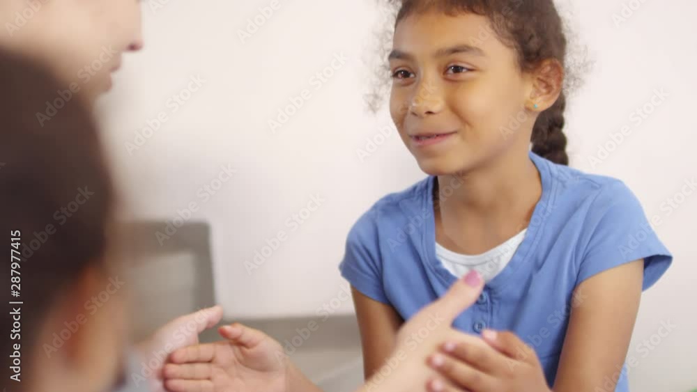 Handheld shot of happy schoolgirl laughing and playing hand game with female teacher during recess Handheld shot of happy schoolgirl laughing and playing hand game with female teacher during recess