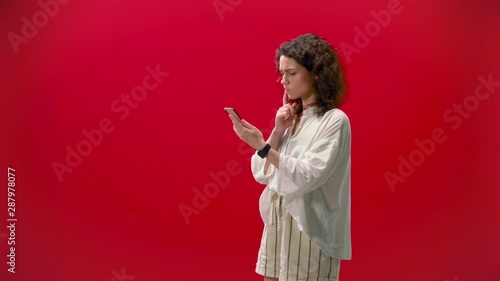 curly girl plays games on an iPhone 11pro in a hand on a red background