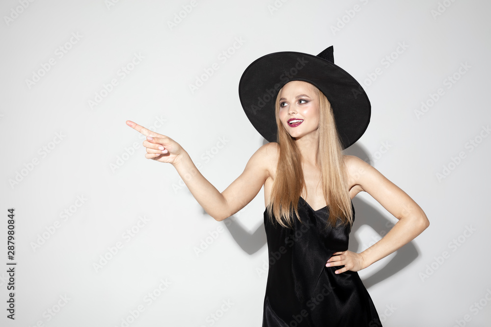 Young blonde woman in black hat and costume on white background. Attractive caucasian female model posing. Halloween, black friday, cyber monday, sales, autumn concept. Copyspace. Pointing, choosing.