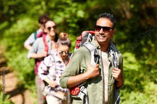 travel, tourism, hike and people concept - group of friends walking with backpacks in forest