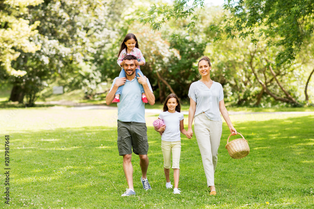 Fototapeta premium family, leisure and people concept - happy mother with picnic basket, father and two daughters walking in summer park