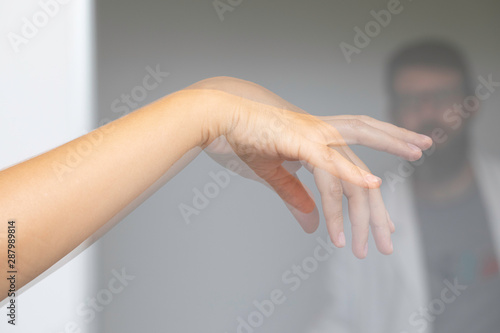 A blurry specialist neurologist physician is seen behind the shuddering hand of a caucasian person, unsteady tremors symptomatic of Parkinson's disease. photo