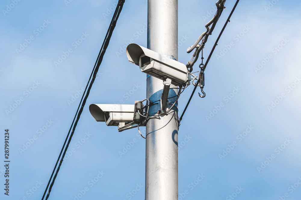 a pair of surveillance cameras on a metal pole against a blue sky a pair of surveillance cameras on a metal pole against a blue sky