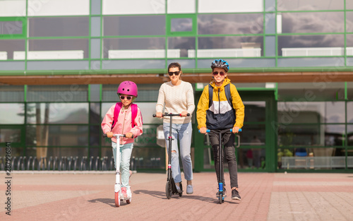 education, school and family concept - happy daughter, son and mother riding scooters outdoors