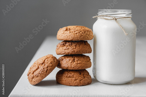 Milk in a glass jar and oatmeal cookies on a white table background. Copy, empty space for text
