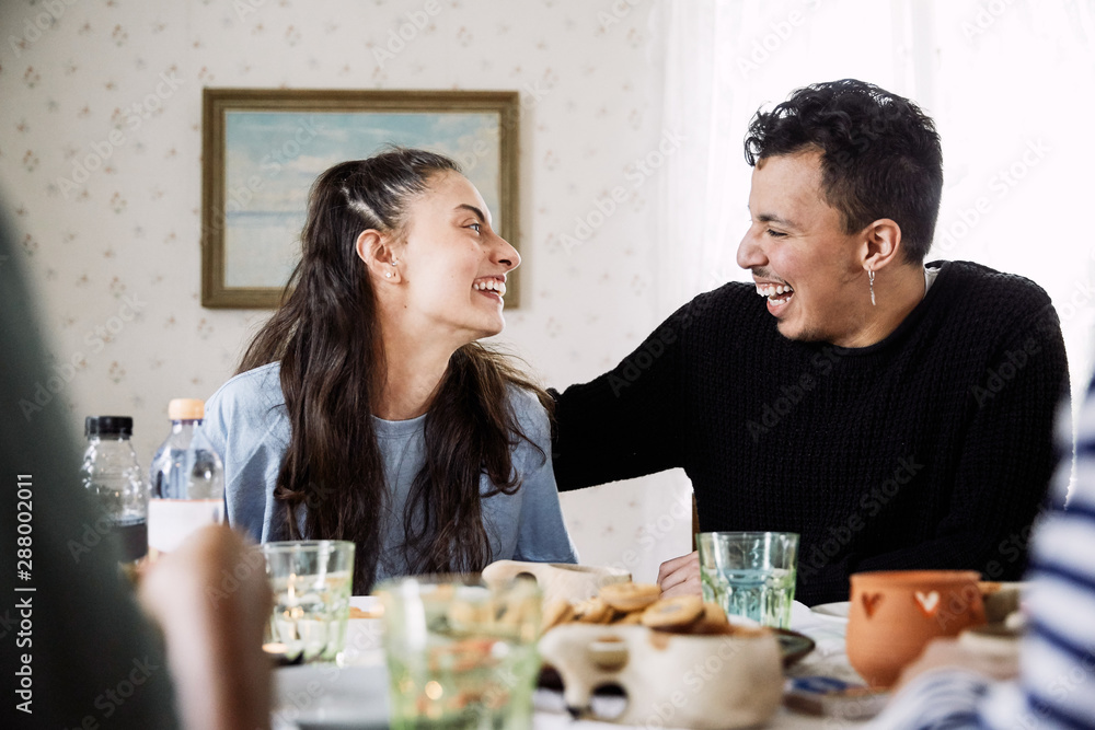 Cheerful friends looking at each other while sitting by food and drink in house Cheerful friends looking at each other while sitting by food and drink in house