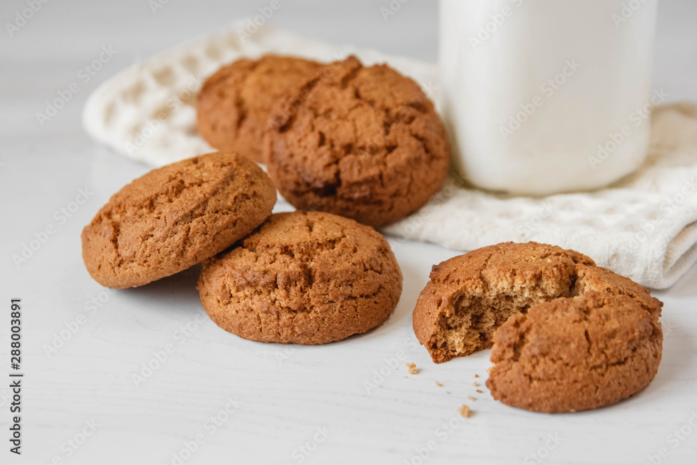 Milk in glass jar and oatmeal cookies near napkin on white table background. Copy, empty space for text Milk in glass jar and oatmeal cookies near napkin on white table background. Copy, empty space for text