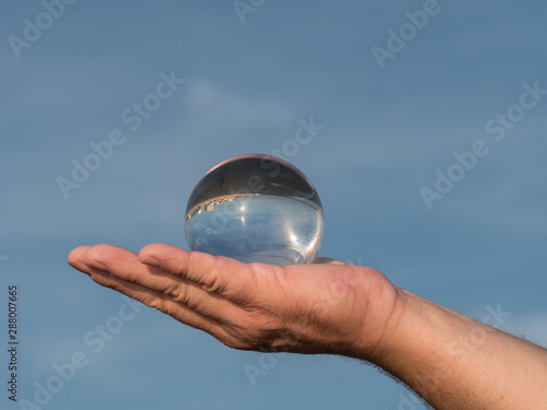 Glaskugel auf einer Hand vor blauem Himmel