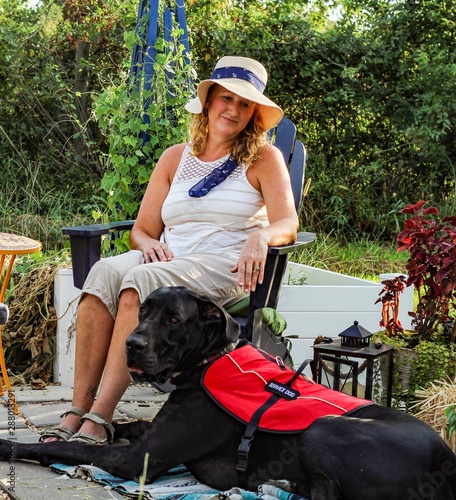 Older adult Caucasian woman with mobility issue is able to enjoy the outdoors on her patio with the help of her loyal and attentive Great Dane service dog by her side