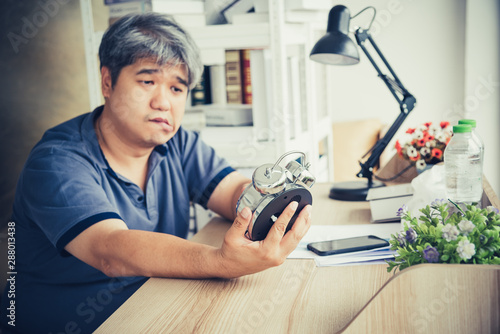 Fotografía Blurred of Asian midle-ages man, He is patient from neurological diseases, or hemiplegia having a facial palsy, He is looking at the alarm clock in his hand, to health and paralysis concept