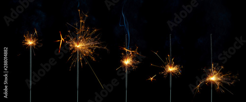 Five lighted sparklers at different stages of burning on a black background. Isolated image.