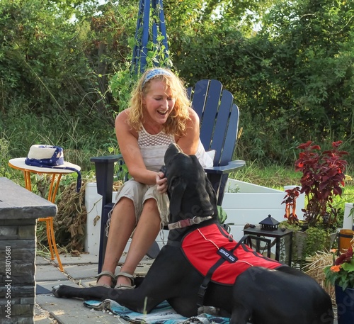 Older adult Caucasian woman with mobility issue is able to enjoy the outdoors on her patio with the help of her loyal and attentive Great Dane service dog by her side