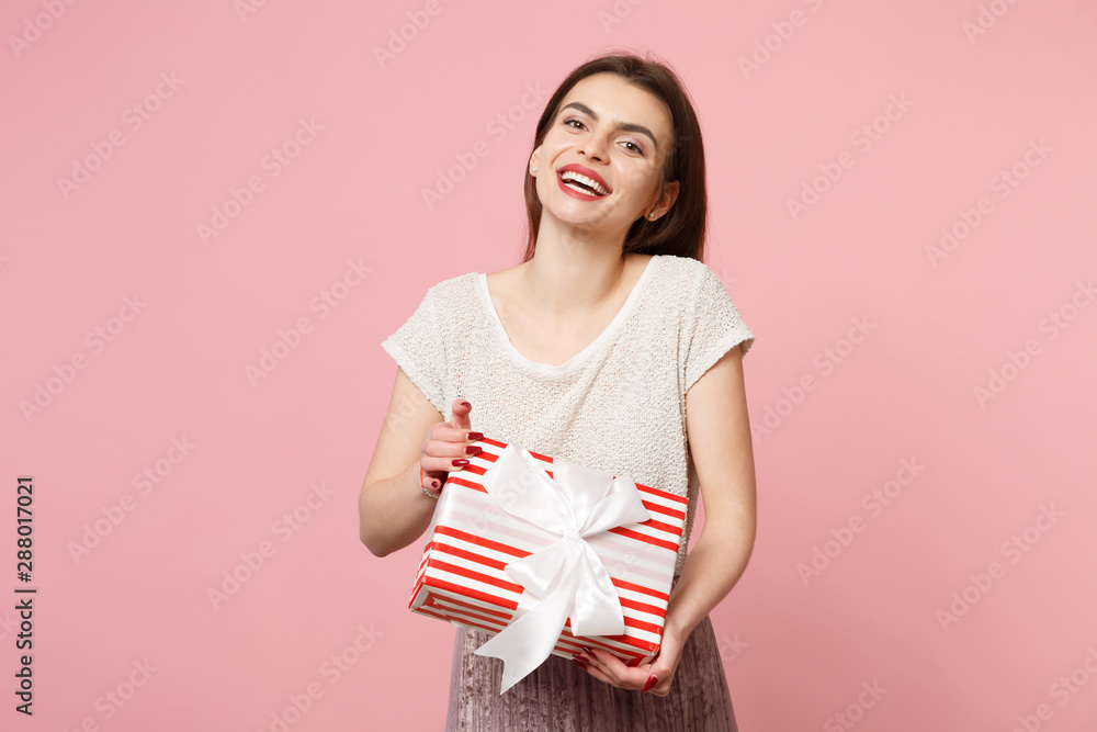 Cheerful young woman in light clothes posing isolated on pink background. Valentine's Day Women's Day birthday, holiday concept. Mock up copy space. Hold red striped present box with gift ribbon bow. Cheerful young woman in light clothes posing isolated on pink background. Valentine's Day Women's Day birthday, holiday concept. Mock up copy space. Hold red striped present box with gift ribbon bow.