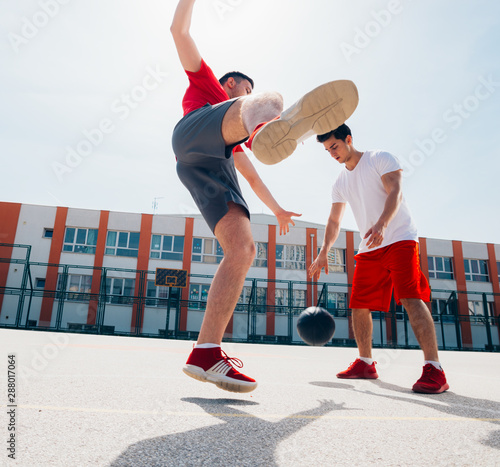 Two Caucasian friends wearing red sports equpment playing basketballs outdoors on a sunny day while they dribble and push each other. photo