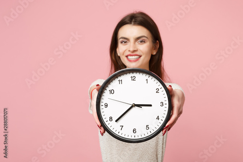 Cheerful young woman in casual light clothes posing isolated on pastel pink wall background, studio portrait. People sincere emotions lifestyle concept. Mock up copy space. Holding in hands clock.