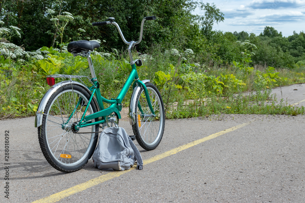 Bicycle and a grey casual backpack standing on asphalt road with yellow line road marking, bike travelling concept Bicycle and a grey casual backpack standing on asphalt road with yellow line road marking, bike travelling concept