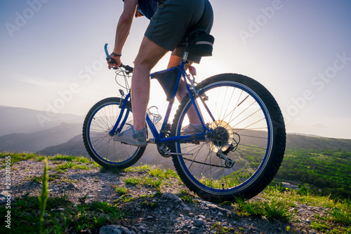 Close up photo from a mountain biker riding his bike ( bicycle) on rough rocky terrain on top of a mountain, wearing no safety equipment. Adrenalin junkie.