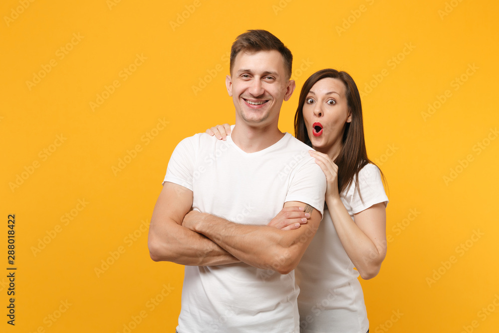 Smiling shocked young couple two friends guy girl in white empty blank design t-shirts posing isolated on yellow orange background. People lifestyle concept. Mock up copy space. Keeping mouth open. Smiling shocked young couple two friends guy girl in white empty blank design t-shirts posing isolated on yellow orange background. People lifestyle concept. Mock up copy space. Keeping mouth open.