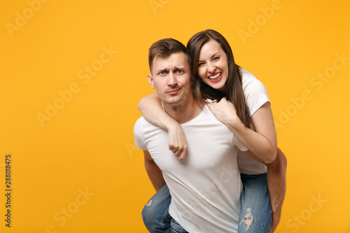 Cheerful young couple two friends guy girl in white t-shirts posing isolated on yellow orange background. People lifestyle concept. Mock up copy space. Giving piggyback ride to joyful sitting on back.