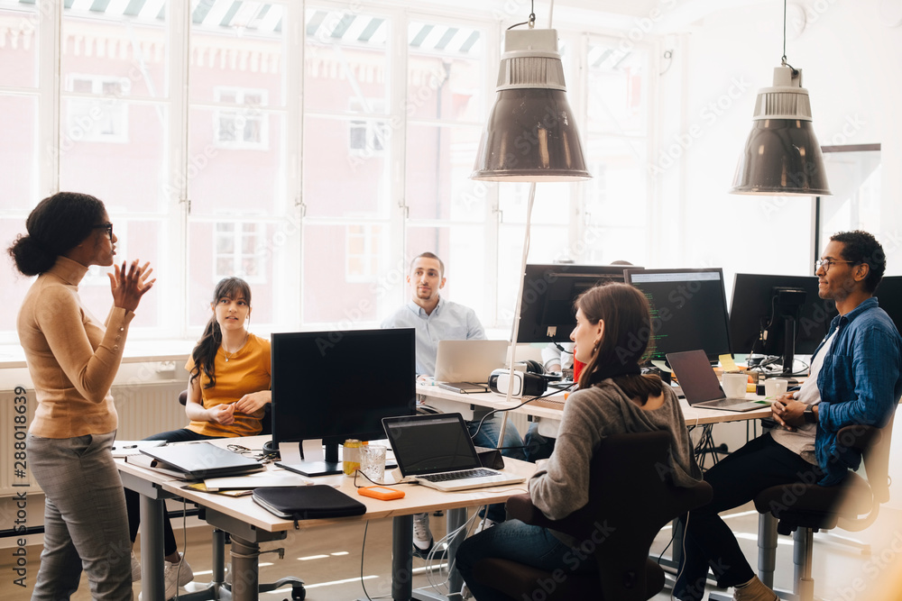 Female computer programmer discussing with coworkers at desk during meeting Female computer programmer discussing with coworkers at desk during meeting