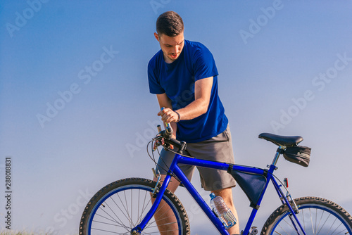 Fit male mountain biker pushing his bike uphill while looking exhausted on a sunny summer day.