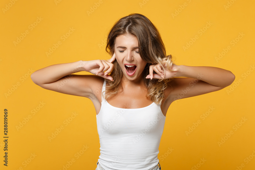 Fototapeta premium Crazy young woman girl in light casual clothes posing isolated on yellow orange background. People lifestyle concept. Mock up copy space. Screaming, keeping eyes closed, covering ears with fingers.