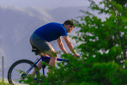 Fototapeta Naklejka Na Ścianę i Meble -  FIt male Cyclist is speeding up his bicycle downhill while enjoying the amazing mountain dirt road.