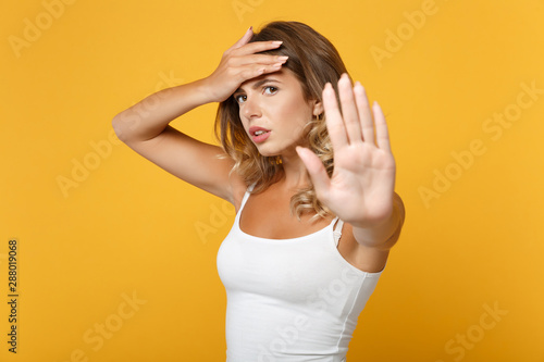 Tired young woman in light casual clothes posing isolated on yellow orange background in studio. People lifestyle concept. Mock up copy space. Showing stop gesture with palm, putting hand on forehead.