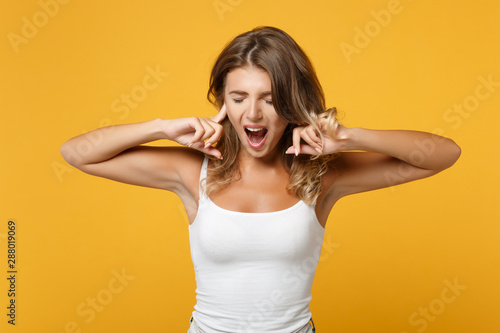 Crazy young woman girl in light casual clothes posing isolated on yellow orange background. People lifestyle concept. Mock up copy space. Screaming, keeping eyes closed, covering ears with fingers.
