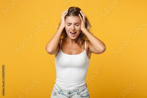 Displeased young woman in light casual clothes posing isolated on yellow orange background, studio portrait. People lifestyle concept. Mock up copy space. Keeping eyes closed, putting hands on head.