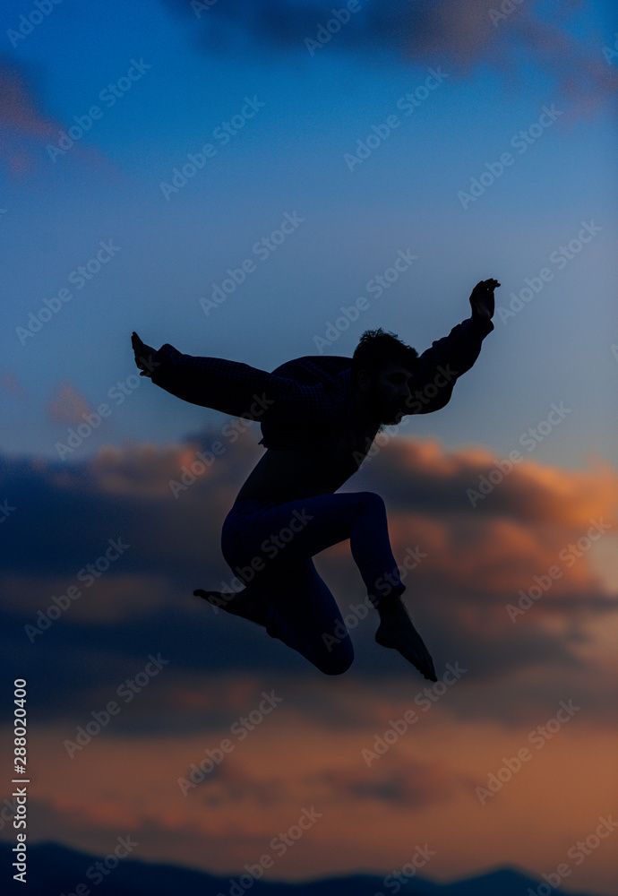Man silhouette performing some moves above blue sky . Mixed media