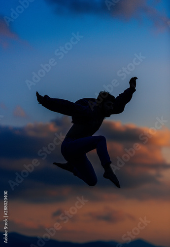 Man silhouette performing some moves above blue sky . Mixed media