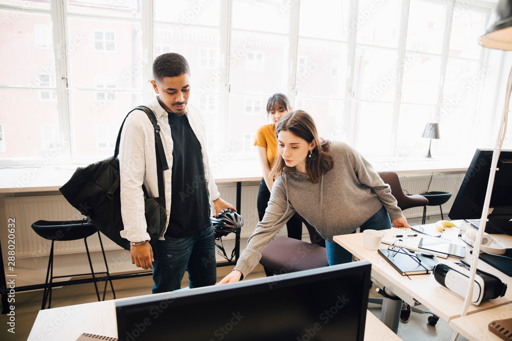 Female programmer showing computer to coworkers against window in ...