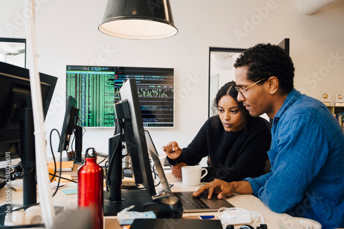 Focused male and female engineers coding over laptop on desk in office photo