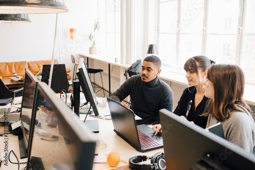 High angle view of IT professionals discussing over laptop on desk in office photo