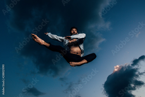 Positive young man is dancing over blue sky