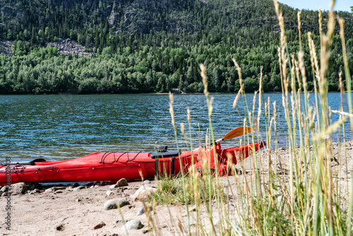 One red colored kayak stranded on the small Island's beach, after paddling from Doksta to Kramfors Island, High Coast, Vasternorrland County Sweden. Grass strows at the right foreground